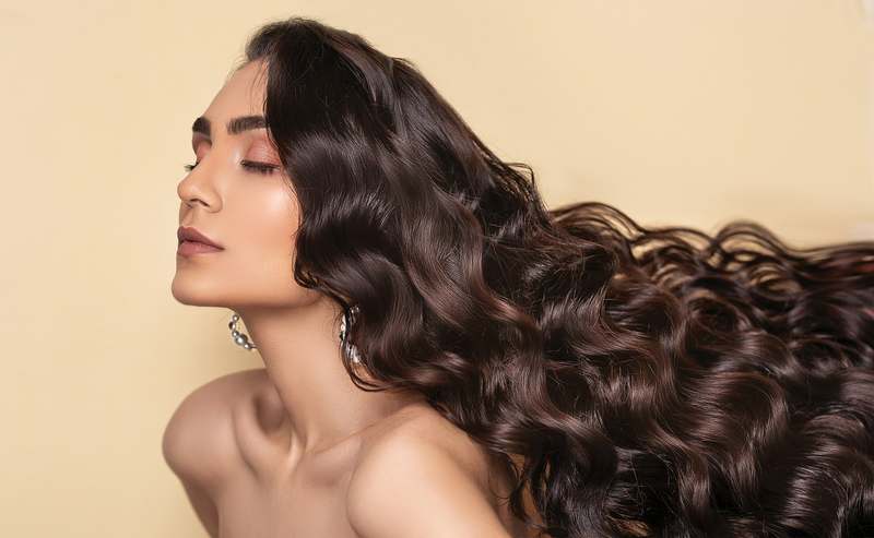 Woman applying hair serum to smooth, shiny brown hair in soft natural light